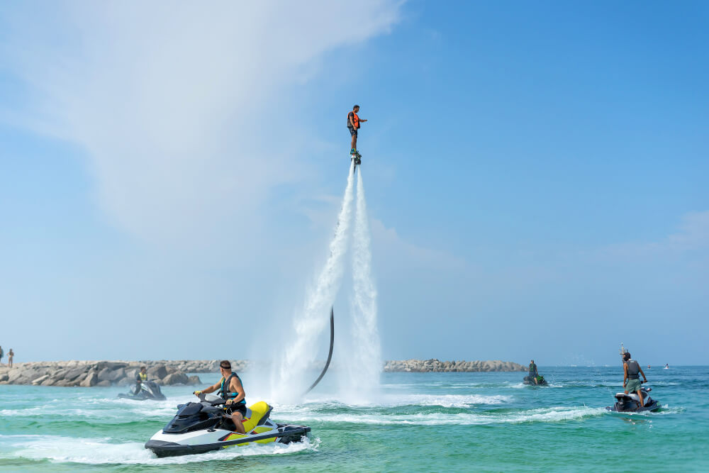 Man on a flyboard without helmet surrounded by wave runners